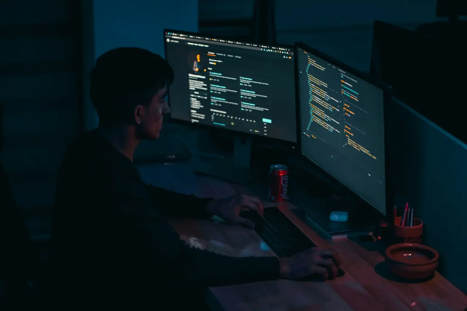 Developer working at dual monitors displaying source code and a web application